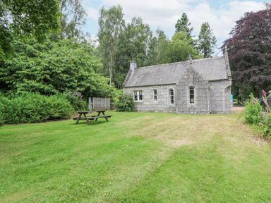 A stone cottage with a slate roof surrounded by grass and trees with a picnic bench outside at East Lodge - Crathes Castle in Crathes Castle near Banchory