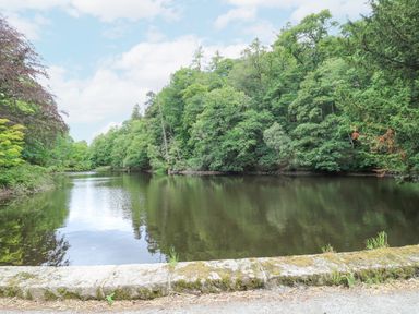 A river surrounded by dense green trees with a stone ledge in the foreground at East Lodge - Crathes Castle in Crathes Castle near Banchory