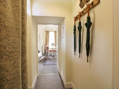 A hallway with three umbrellas hanging on the wall leading to a room with a dining table and chairs at East Lodge - Crathes Castle in Crathes Castle near Banchory