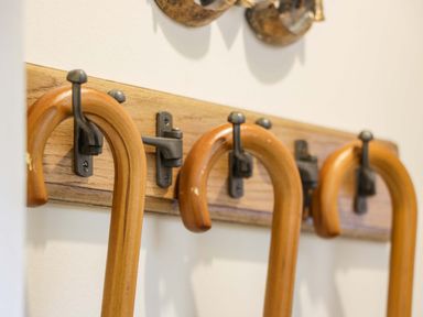 Wooden canes hanging on metal hooks attached to a wooden board on a white wall at East Lodge - Crathes Castle in Crathes Castle near Banchory