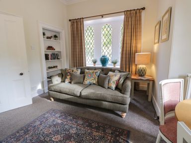 A living room with a sofa with patterned cushions a table with a lamp a bookshelf and a window with curtains at East Lodge - Crathes Castle Crathes Castle near Banchory