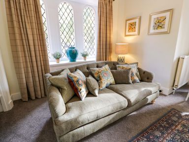 A sofa with patterned cushions in front of a window with beige curtains a lamp on a side table and framed pictures on the wall at East Lodge - Crathes Castle Crathes Castle near Banchory