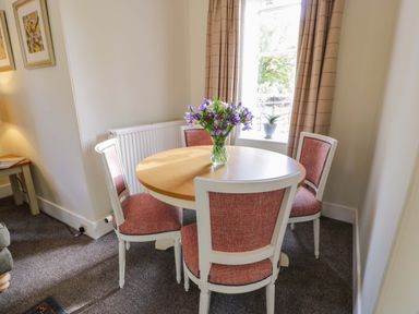 A dining area with a round wooden table and four upholstered chairs near a window with beige curtains at East Lodge - Crathes Castle in Crathes Castle near Banchory
