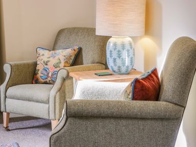 Two armchairs with floral and solid color cushions next to a wooden side table with a patterned lamp on it at East Lodge - Crathes Castle in Crathes Castle near Banchory