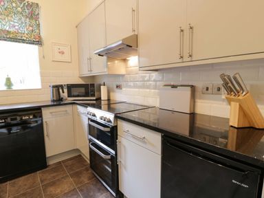 A kitchen with white cabinets black appliances and a tiled backsplash at East Lodge - Crathes Castle in Crathes Castle near Banchory
