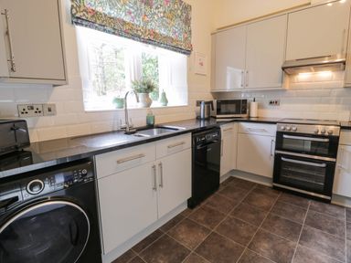 A kitchen with white cabinets black appliances and a floral curtain at East Lodge Crathes Castle near Banchory