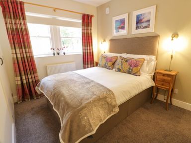A bedroom with a double bed two bedside tables with lamps curtains on the window and paintings above the bed at East Lodge - Crathes Castle in Crathes Castle near Banchory