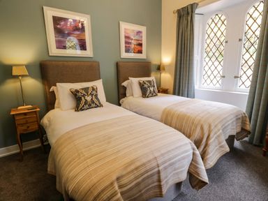 A bedroom with two single beds bedside tables lamps and framed pictures on the wall at East Lodge - Crathes Castle in Crathes Castle near Banchory