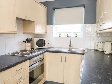 A kitchen with wooden cabinets a microwave a sink a stove a toaster and a kettle at 91 Waterside Park in Lowestoft