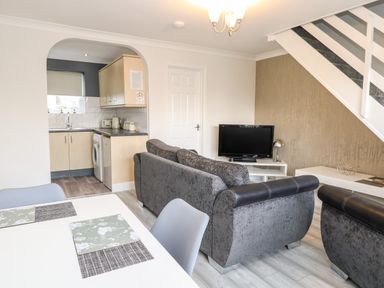 A living room with grey sofas a television and a dining table next to a kitchen at 91 Waterside Park in Lowestoft