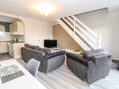 A living room with grey sofas a TV on a stand and a staircase next to an open kitchen at 91 Waterside Park in Lowestoft