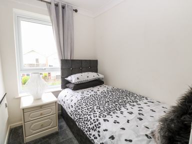A small bedroom with a single bed a bedside table with a lamp and a window with curtains at 91 Waterside Park in Lowestoft