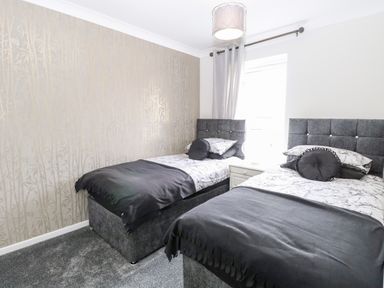 A bedroom with two single beds with grey headboards black throws and a white nightstand between the beds at 91 Waterside Park in Lowestoft