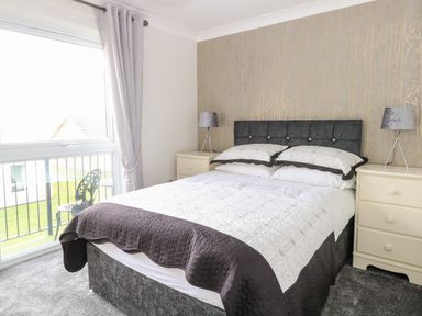A bedroom with a bed between two nightstands with lamps and a window with curtains at 91 Waterside Park in Lowestoft