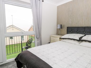 A bedroom with a bed side table lamp and a window showing outdoor chairs at 91 Waterside Park in Lowestoft