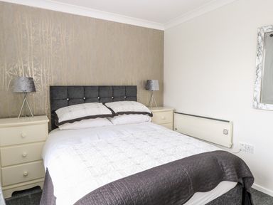 A bedroom with a double bed two bedside tables and lamps a heater and a wall mirror at 91 Waterside Park in Lowestoft