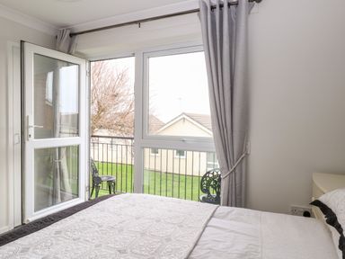 A bedroom with a bed facing a glass door leading to a small balcony with chairs at 91 Waterside Park in Lowestoft