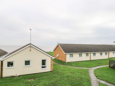 Two single-story buildings with windows near a grassy area and a curved sidewalk by the sea at 91 Waterside Park in Lowestoft