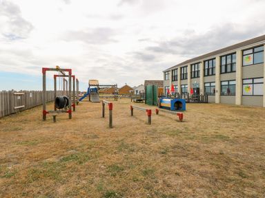 An outdoor playground with climbing structures slides and swings next to a two story building at 91 Waterside Park in Lowestoft