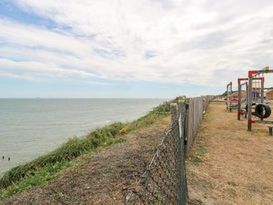 A coastal path with a fence separating grassy areas and a playground near the sea at 91 Waterside Park in Lowestoft
