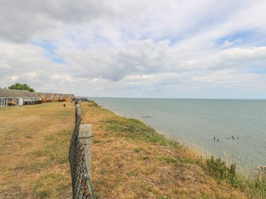 A seaside view with a row of houses on the left and a grassy cliff overlooking the ocean at 91 Waterside Park in Lowestoft