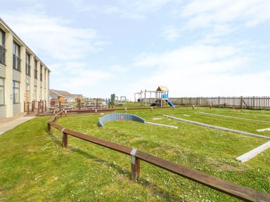 An outdoor area with picnic tables a children's play area and a fenced grass field at 91 Waterside Park in Lowestoft