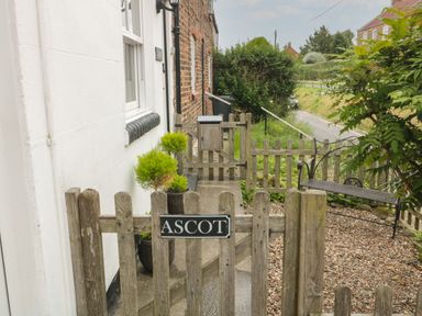 A wooden gate with a sign reading Ascot leading to a garden path with potted plants and a bench at Ascot Cottage in Sheriff Hutton near Strensall