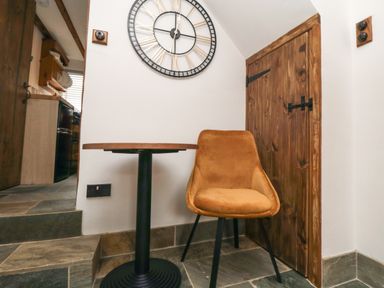 A corner with a small round table and an orange chair near a wooden door and a large wall clock at Ascot Cottage in Sheriff Hutton near Strensall