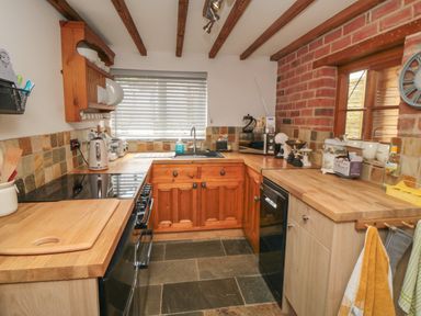 A kitchen with wooden cabinets and countertops a stove a sink and brick walls at Ascot Cottage Sheriff Hutton near Strensall