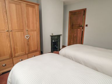 A bedroom with two single beds a wooden wardrobe a wooden door and a small black fireplace at Ascot Cottage in Sheriff Hutton near Strensall