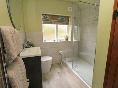 A bathroom with a sink cabinet a toilet a glass shower enclosure towels and a window with a floral blind at Ascot Cottage in Sheriff Hutton near Strensall