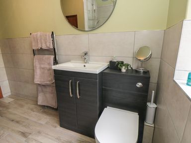 A bathroom with a sink cabinet toilet towel rack round mirror and small round vanity mirror at Ascot Cottage Sheriff Hutton near Strensall