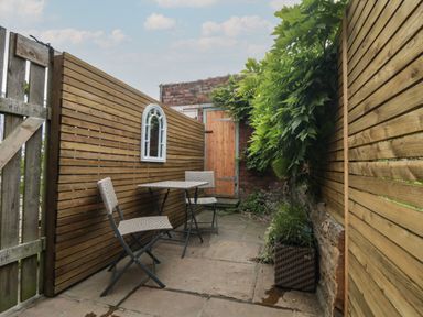 An outdoor patio area with two chairs and a table between wooden fences and a wooden gate at Ascot Cottage in Sheriff Hutton near Strensall