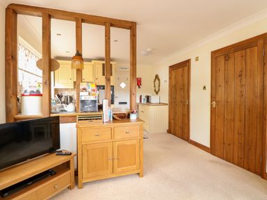 A living area with wooden furniture a television and a view into a kitchen at Hunters Lodge Great Moulton near Long Stratton