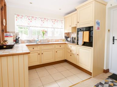 A kitchen with cream cabinets tiled countertops and a window with floral blinds at Hunters Lodge in Great Moulton near Long Stratton
