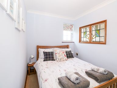 A bedroom with a wooden bed with pillows and towels on it with two windows one with stained glass at Hunters Lodge in Great Moulton near Long Stratton