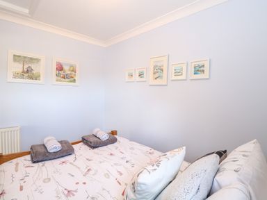 A bedroom with a bed covered in floral bedding two gray towels and rolled white towels on top and framed artwork on the walls at Hunters Lodge in Great Moulton near Long Stratton