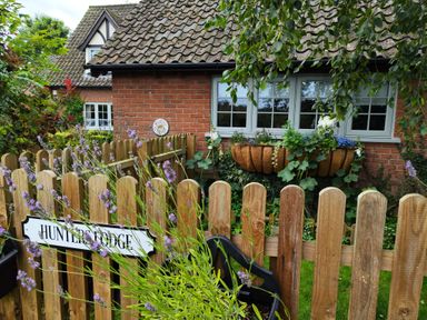 A brick house with windows flower boxes and a wooden fence with a sign saying Hunters Lodge Great Moulton near Long Stratton