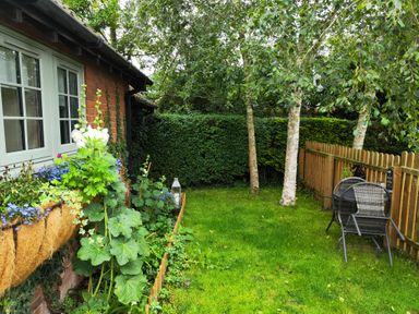 A garden with green grass trees wooden fence and two garden chairs at Hunters Lodge in Great Moulton near Long Stratton