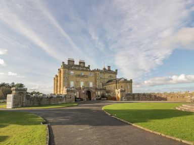 A historic castle building with stone walls and a paved driveway surrounded by grass at Ardlochan Lodge - Culzean Castle in Maybole