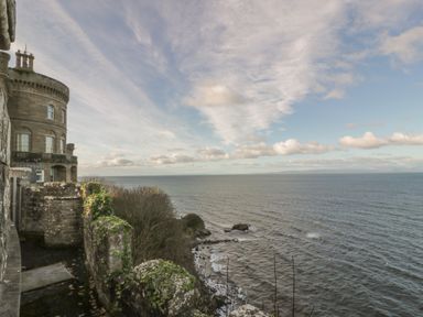 A stone castle overlooking a rocky coastline and sea under a cloudy sky at Ardlochan Lodge - Culzean Castle in Maybole