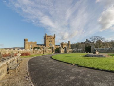A stone castle with a clock tower surrounded by a stone wall and green lawn at Ardlochan Lodge - Culzean Castle in Maybole