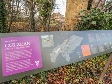 An outdoor information board with a map and welcome text for Culzean Castle and Country Park surrounded by trees and greenery