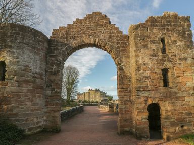 A stone archway with castle ruins and a large building in the background at Ardlochan Lodge - Culzean Castle in Maybole