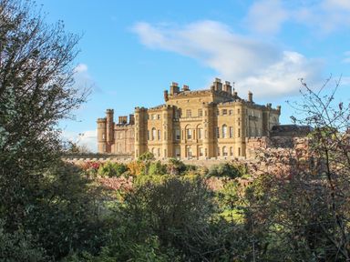 A large stone castle with multiple turrets and chimneys surrounded by trees and garden at Ardlochan Lodge - Culzean Castle in Maybole
