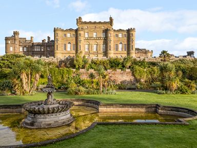 A castle with cylindrical towers behind a garden with a fountain and green grass at Ardlochan Lodge - Culzean Castle in Maybole