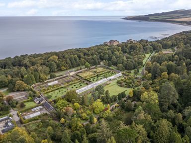Aerial view of a garden with greenhouses and trees near a castle and coastline at Ardlochan Lodge - Culzean Castle in Maybole
