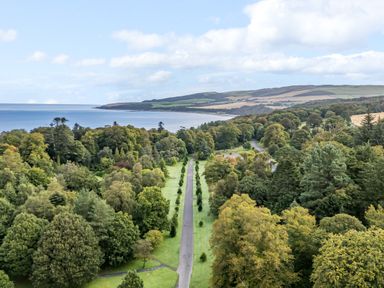 A long road lined with trees leading to a coastline with hills and water at Ardlochan Lodge - Culzean Castle in Maybole