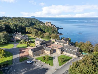 A coastal property complex with stone buildings near a castle on a cliff surrounded by trees and water at Ardlochan Lodge - Culzean Castle in Maybole