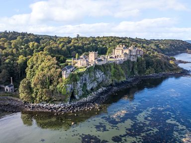 A castle on a rocky coastline surrounded by trees and water at Ardlochan Lodge - Culzean Castle in Maybole